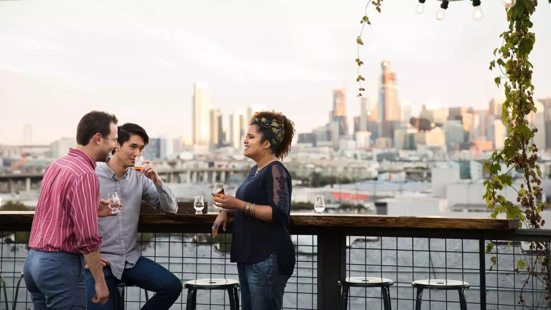 Três pessoas se reúnem em torno de uma mesa ao ar livre na cobertura da Anchor Distilling em São Francisco, Califórnia.