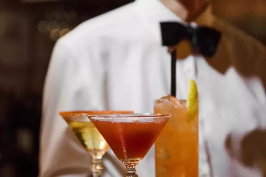 在贝博体彩app的苦艾酒餐厅，一个戴着领结的服务员展示了一盘鸡尾酒.