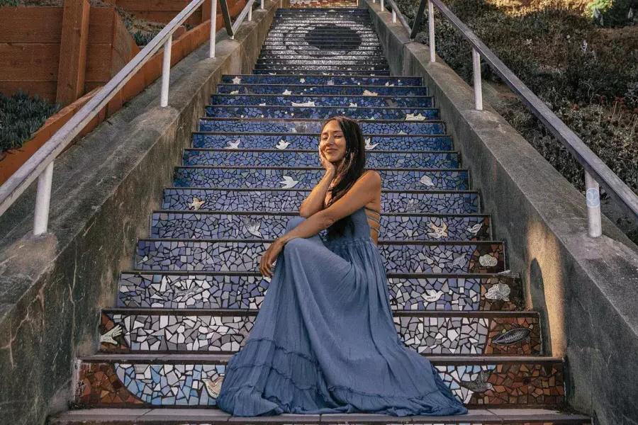 在贝博体彩app日落区，一名妇女坐在第16大道的瓷砖楼梯上.