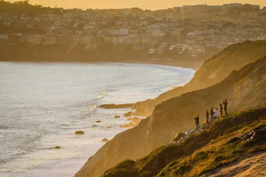 一群人站在面向大海的悬崖上，凝视着贝博体彩app要塞的日落.